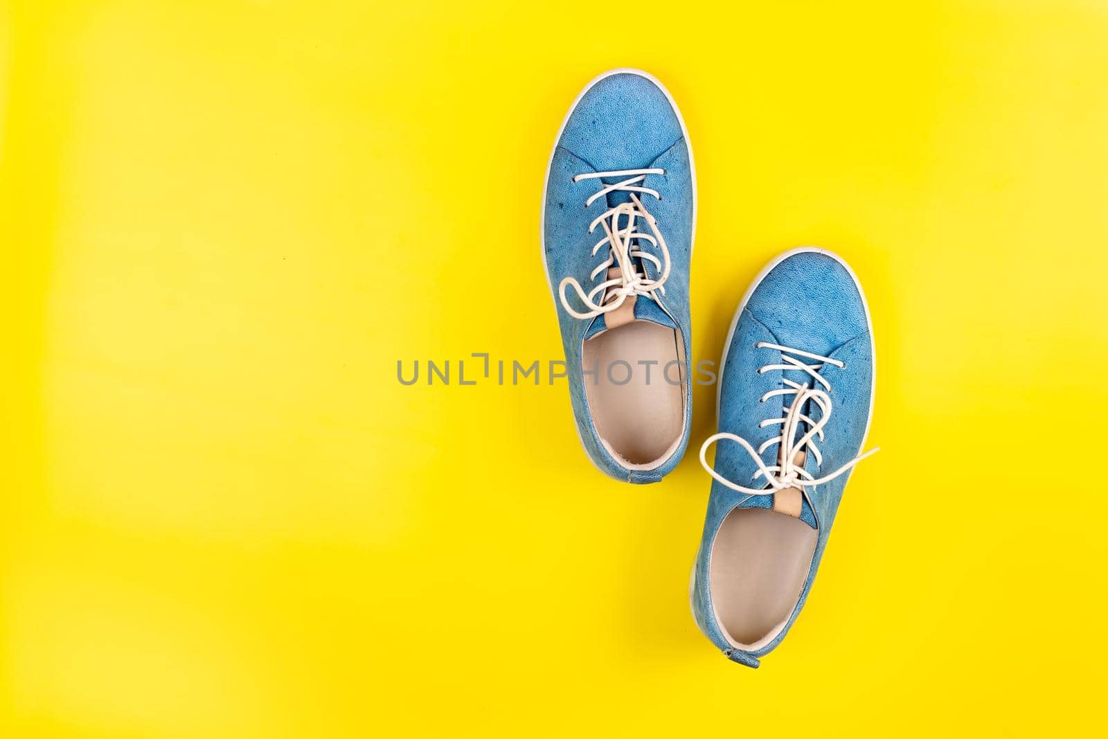 Blue shoes stand on an isolated yellow background by Lobachad