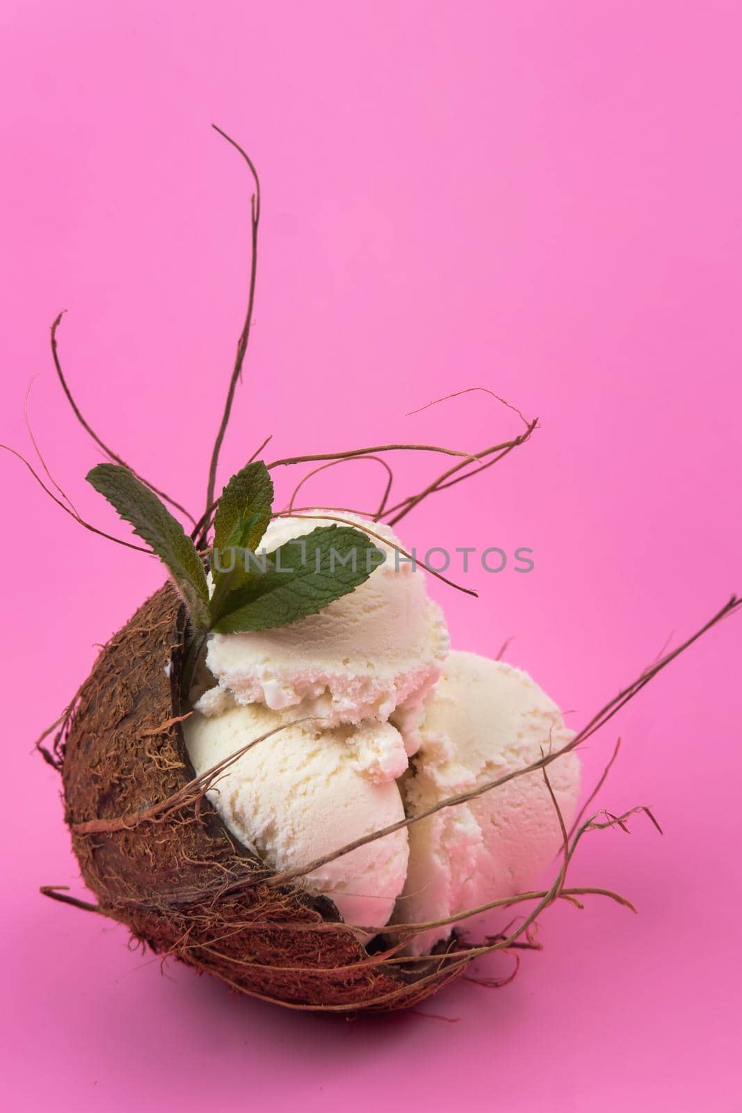 Vanilla ice cream balls in an empty coconut decorated with mint leaves on a pink background.