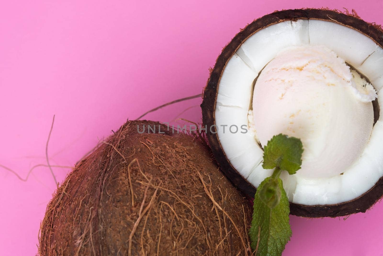 Vanilla ice cream balls in fresh coconut halves decorated with mint leaves on a pink background.