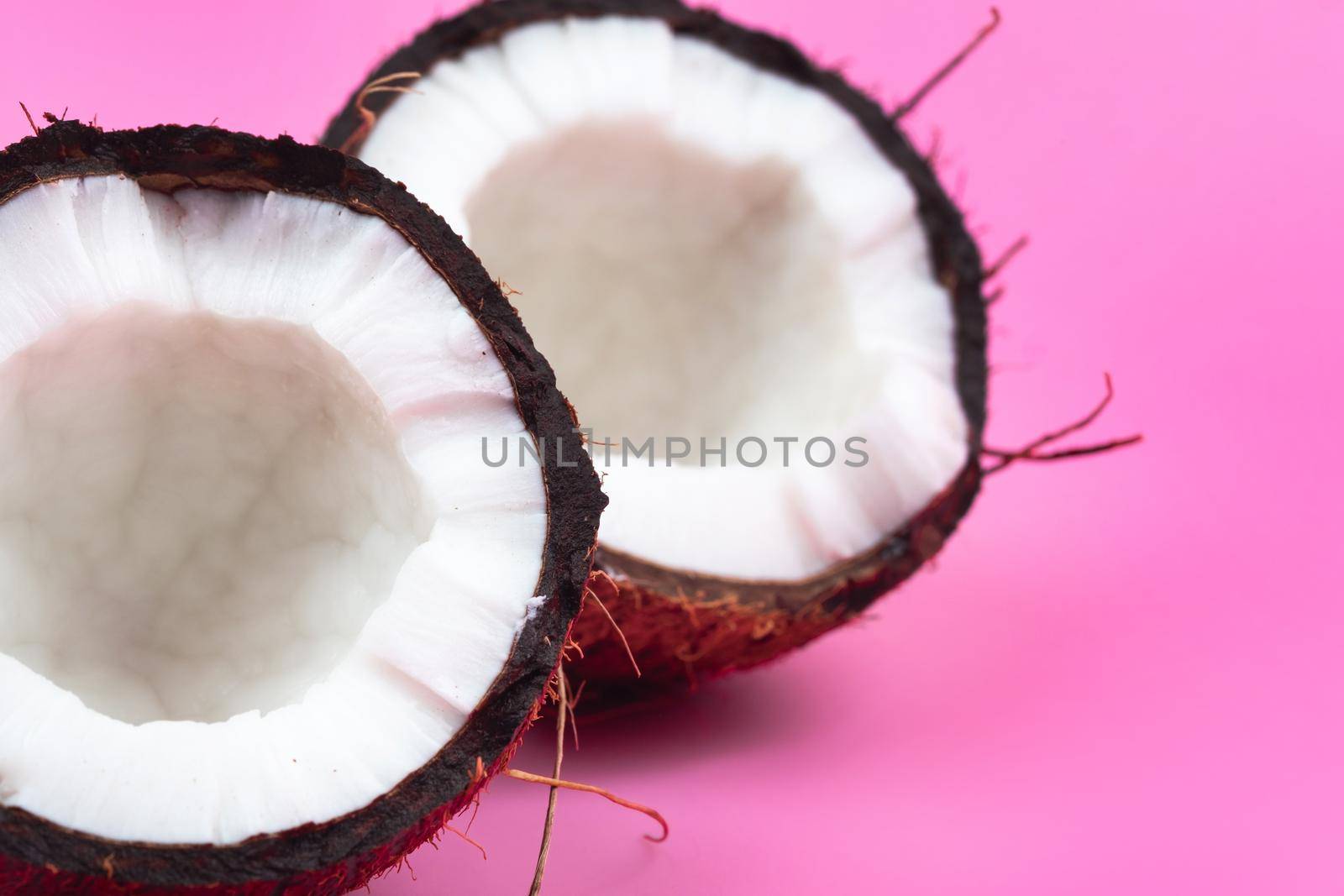 Two halves of a ripe coconut with white flesh on a pink background. by Lobachad