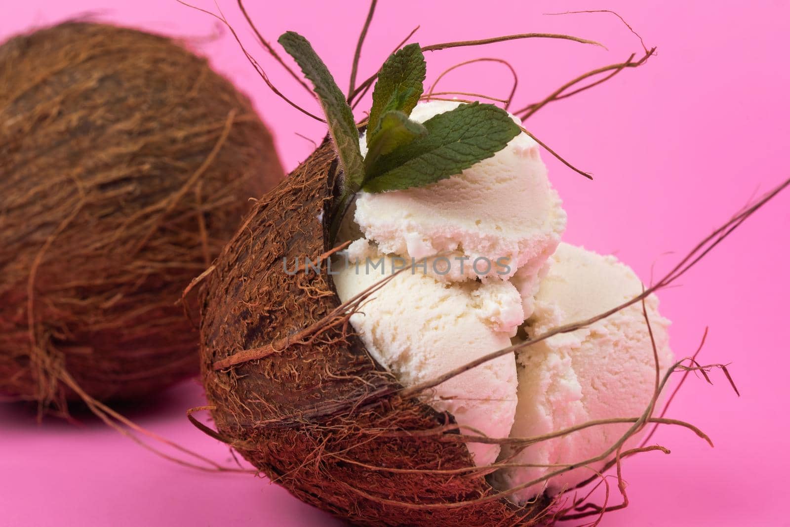 Vanilla ice cream balls in an empty coconut decorated with mint leaves on a pink background.