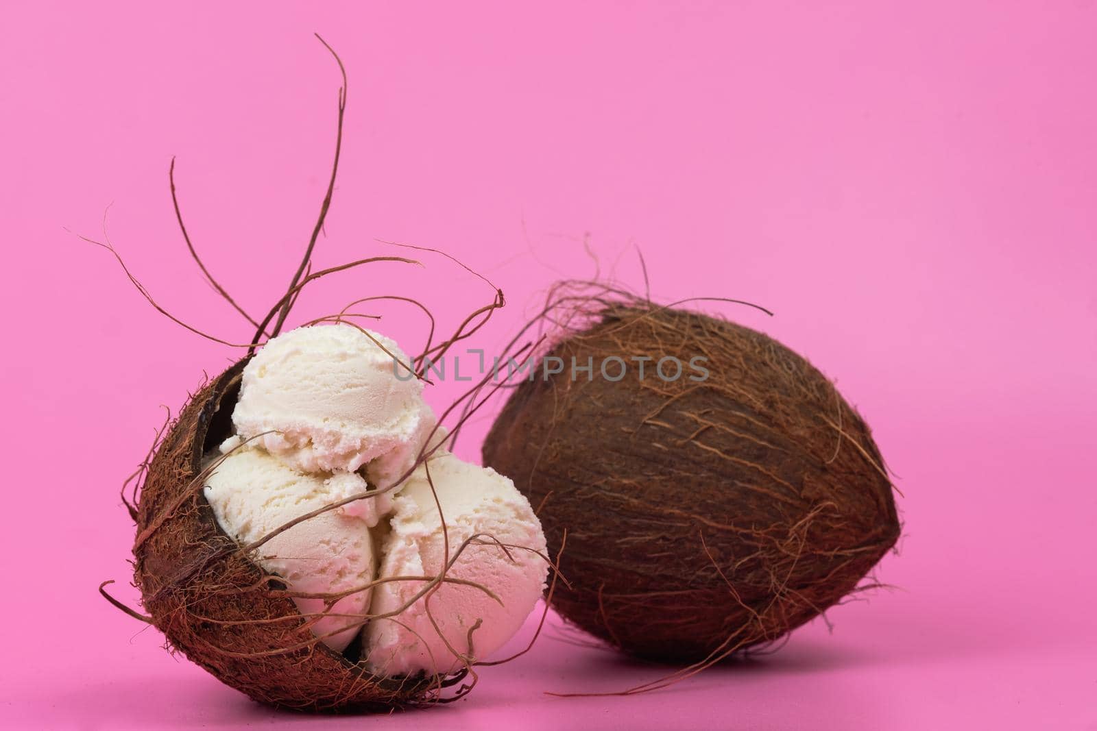 Vanilla ice cream balls in an empty coconut decorated with mint leaves on a pink background by Lobachad