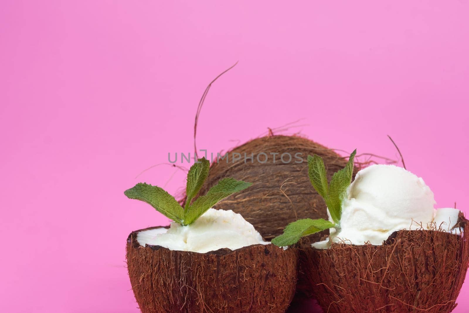 Vanilla ice cream balls in fresh coconut halves decorated with mint leaves on a pink background.