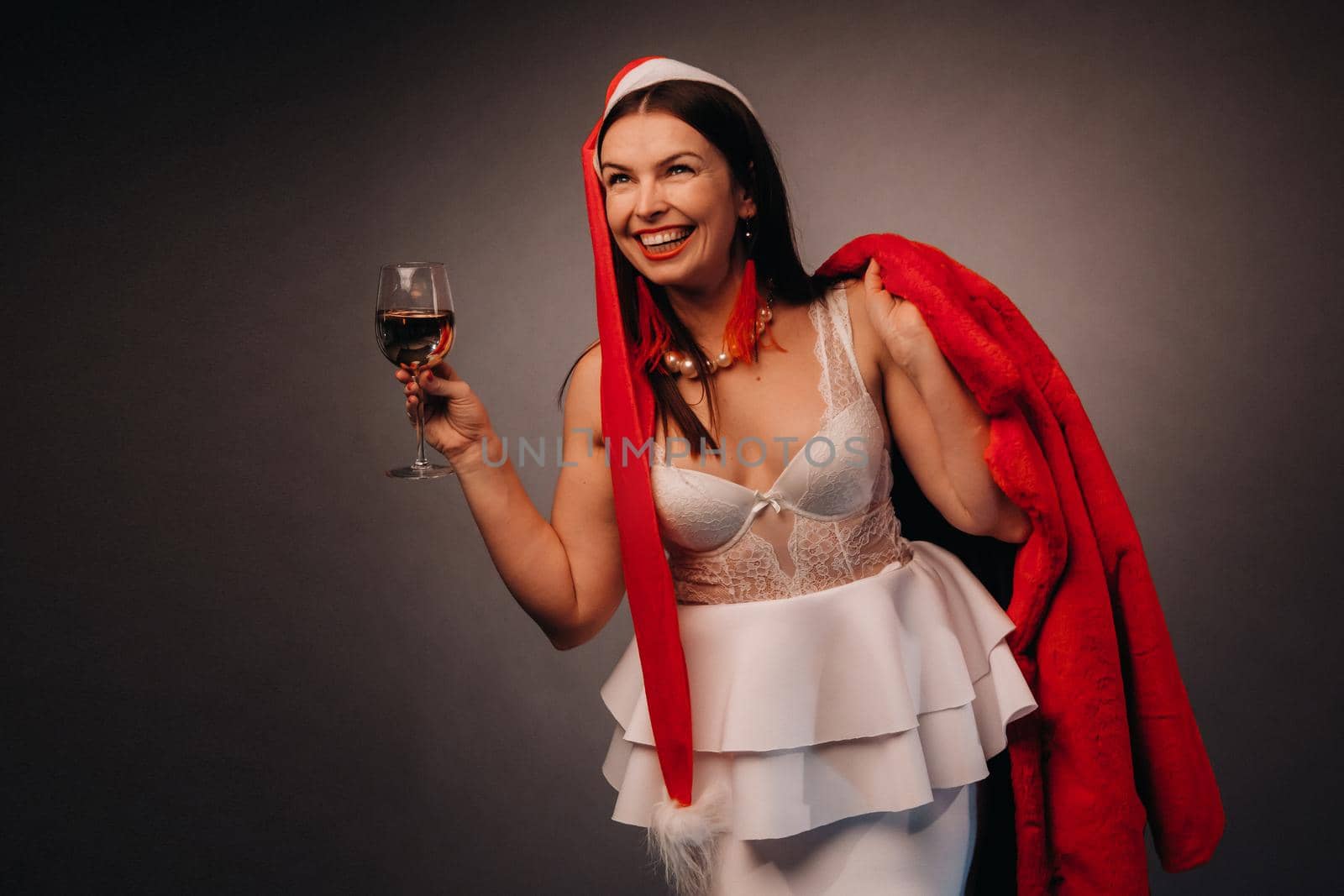 a woman in a Christmas hat and white dress, holding a glass and a red fur coat in her hands, on a black background, Christmas, holiday by Lobachad