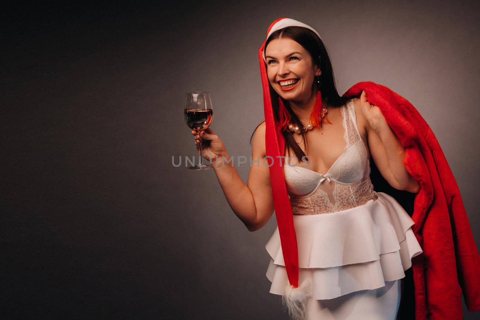 a woman in a Christmas hat and white dress, holding a glass and a red fur coat in her hands, on a black background, Christmas, holiday by Lobachad