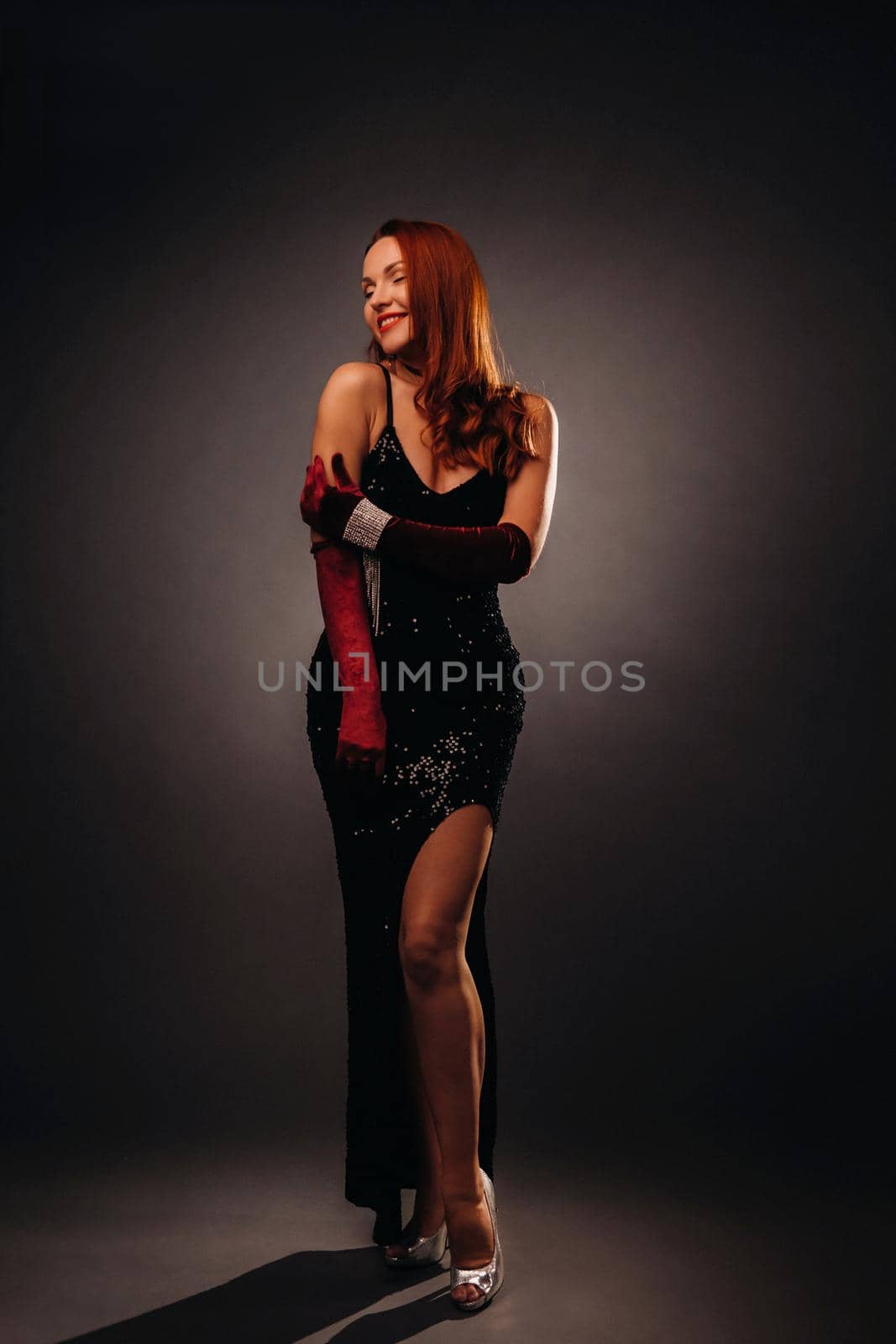 Red-haired girl in a black dress and elegant gloves on a black background.