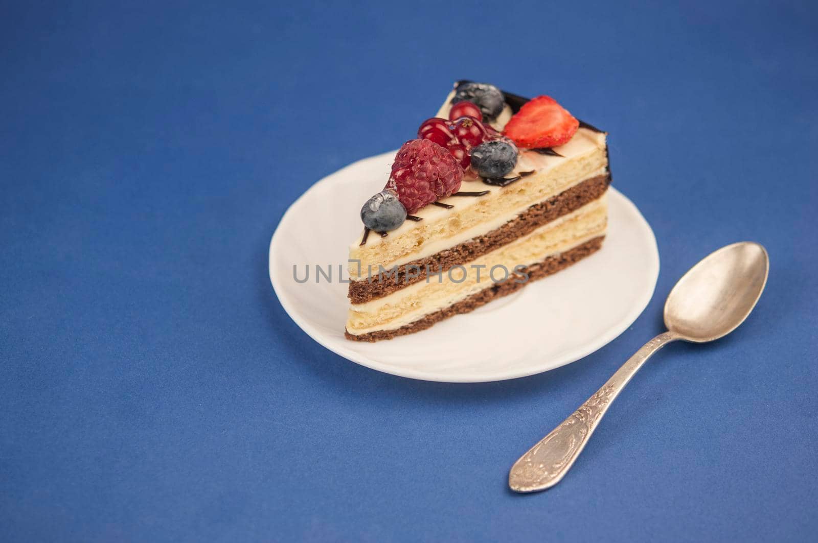 Mix berry slice cake on plate with vintage spoon on soft blue paper background. Good morning. Breakfast