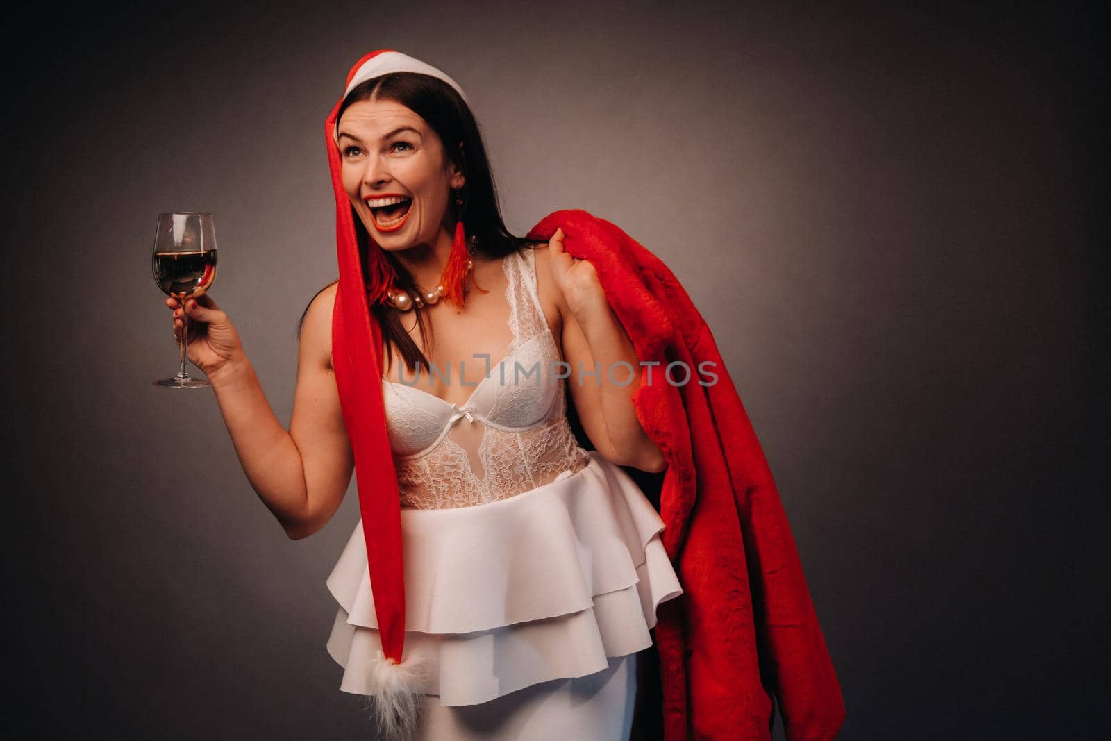 a woman in a Christmas hat and white dress, holding a glass and a red fur coat in her hands, on a black background, Christmas, holiday by Lobachad