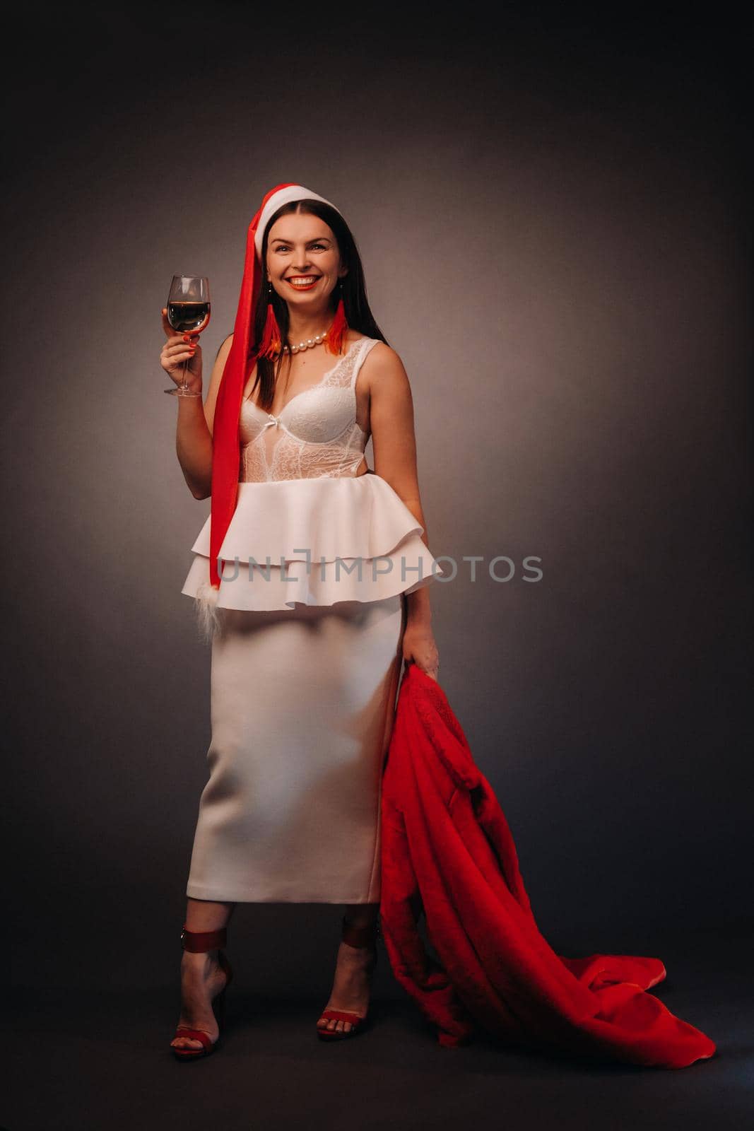 a woman in a Christmas hat and white dress, holding a glass and a red fur coat in her hands, on a black background, Christmas, holiday,