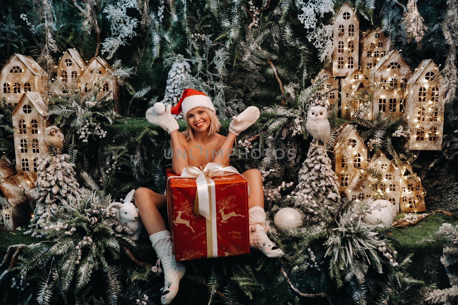 a girl in a Santa hat with a big Christmas gift in her hands on a fabulous Christmas background.Smiling woman in a bathing suit on the background of Christmas trees and small houses.
