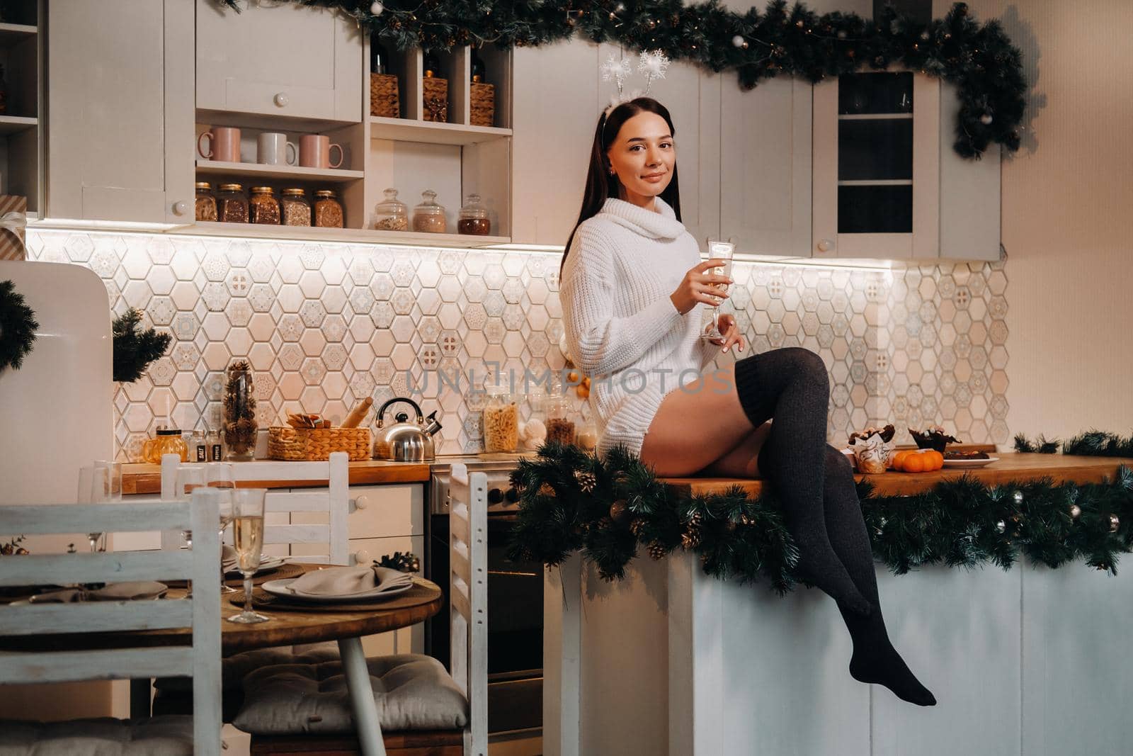 A girl on Christmas day is sitting on the kitchen table and holding a glass of champagne.Woman on new year's eve with champagne.