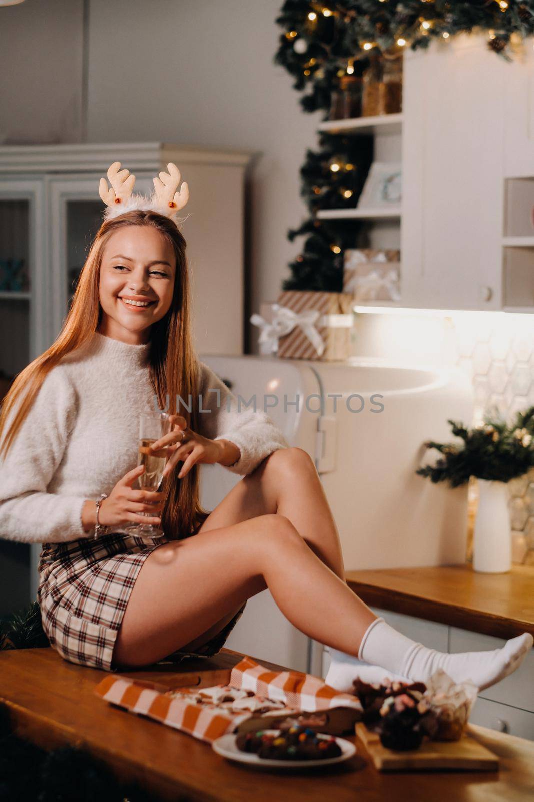 A girl on Christmas day sits on the kitchen table and holds a glass of champagne in her hands.A woman on New year's eve in the kitchen with champagne.