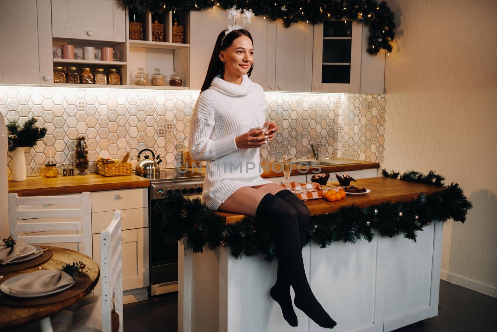 A girl at Christmas is sitting on the table in the kitchen, holding a cake and dreaming.A woman on New year's eve in the kitchen.