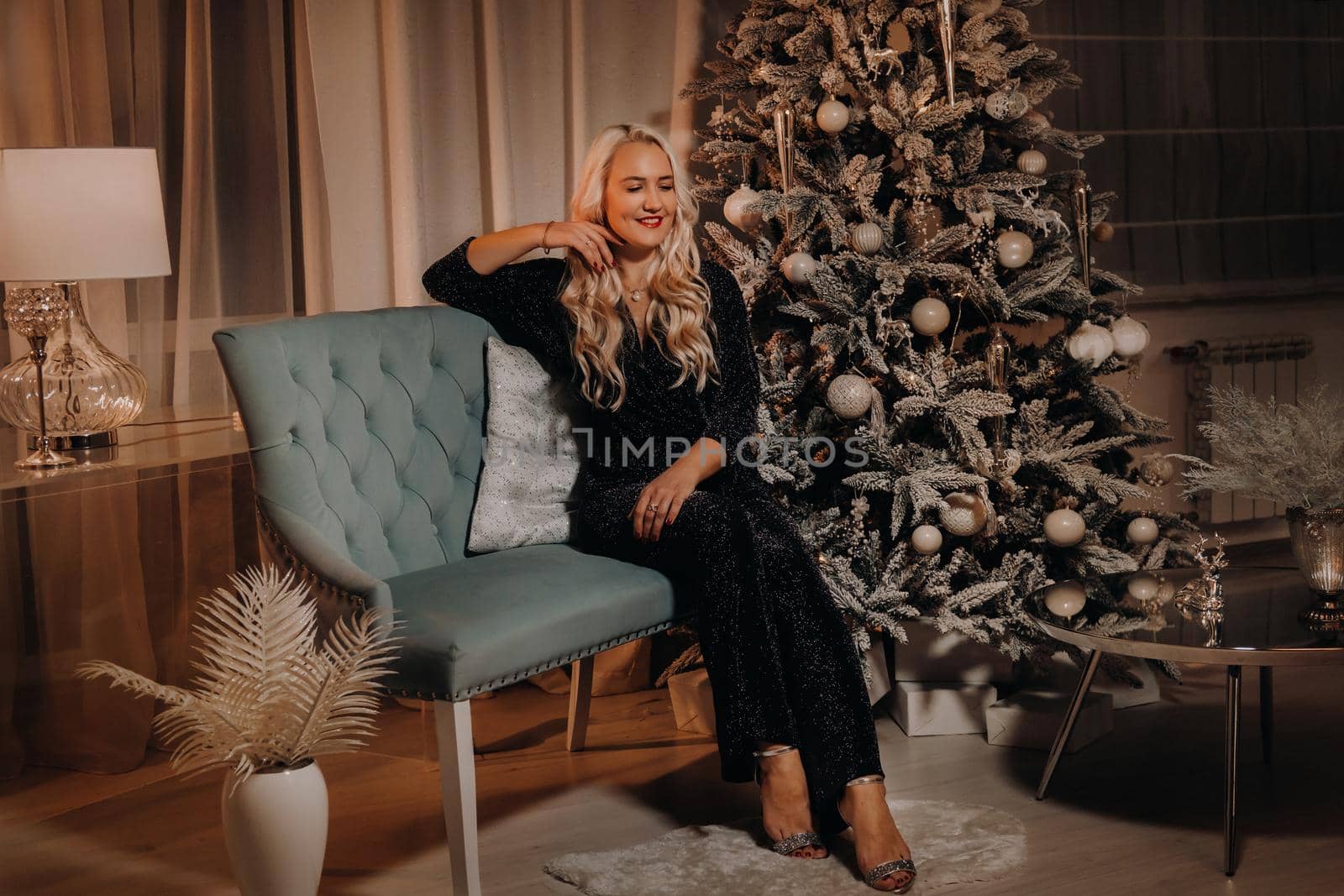 A girl in an evening dress is sitting on the sofa near the Christmas tree.