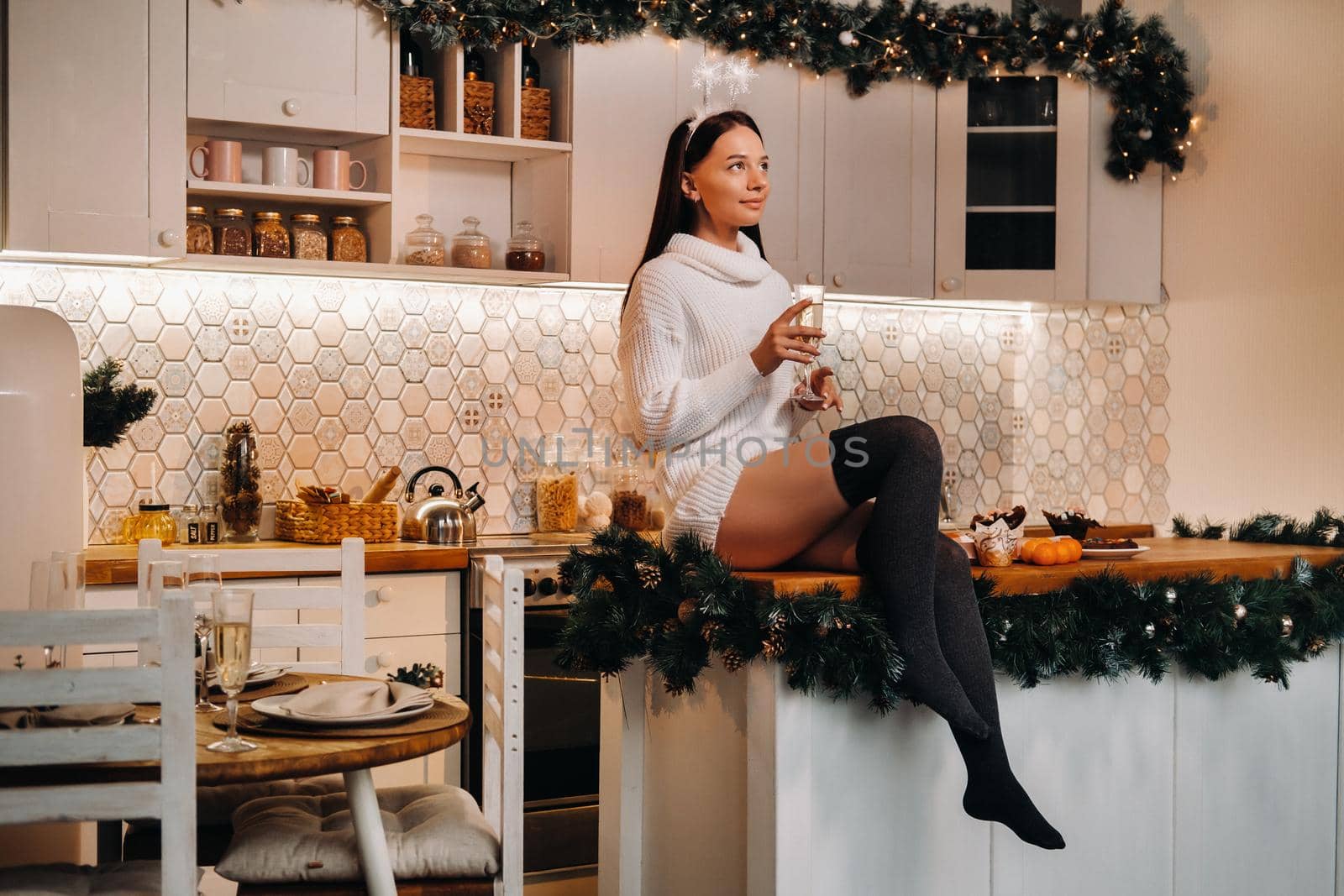 A girl on Christmas day is sitting on the kitchen table and holding a glass of champagne.Woman on new year's eve with champagne.