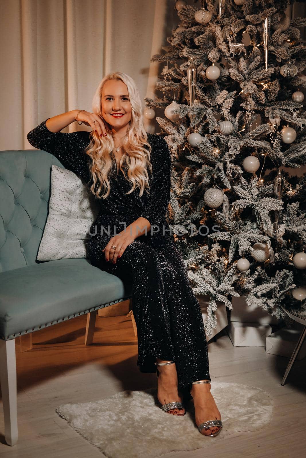 A girl in an evening dress is sitting on the sofa near the Christmas tree.