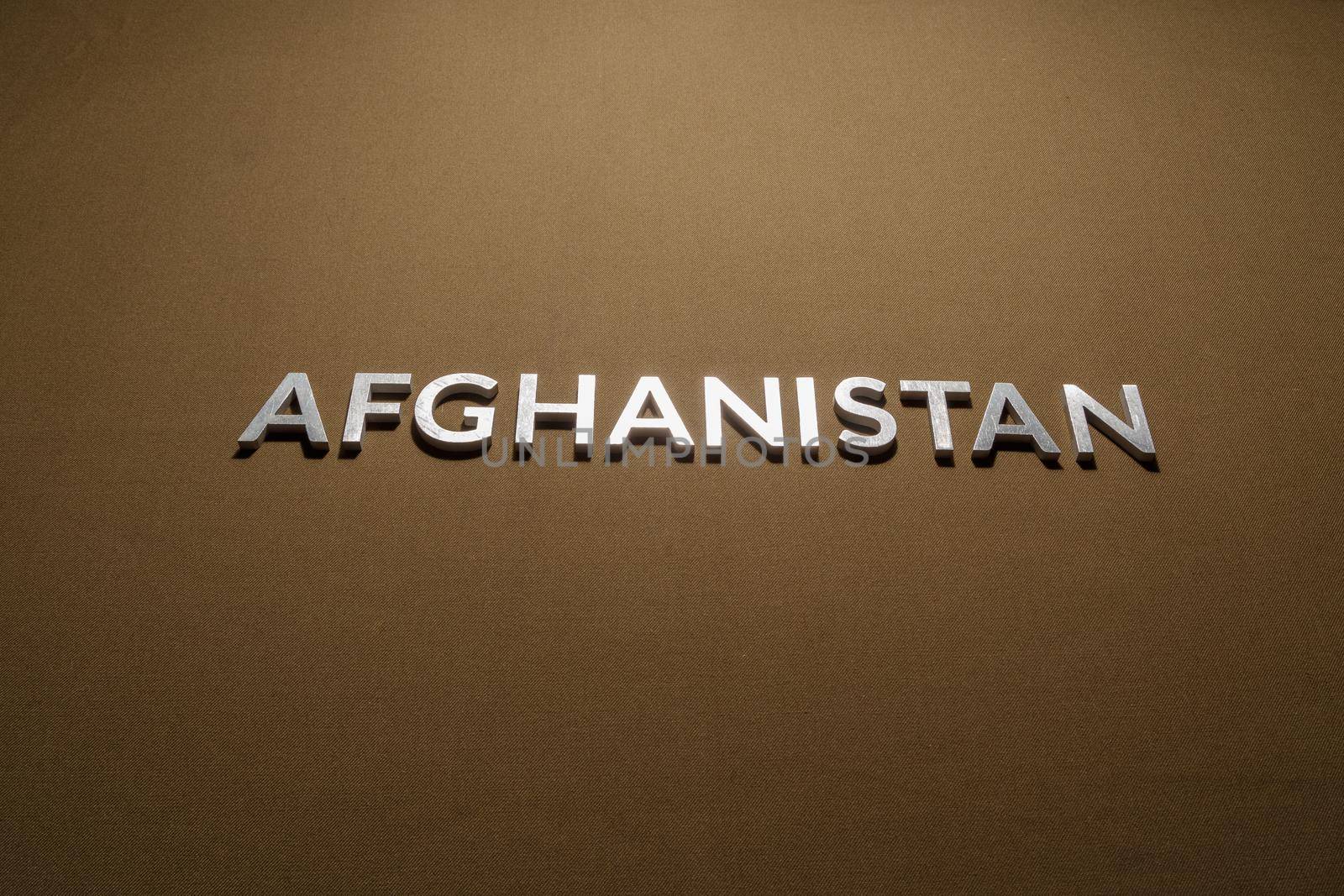 the word afghanistan laid with silver metal letters on rough flat tan khaki canvas fabric surface