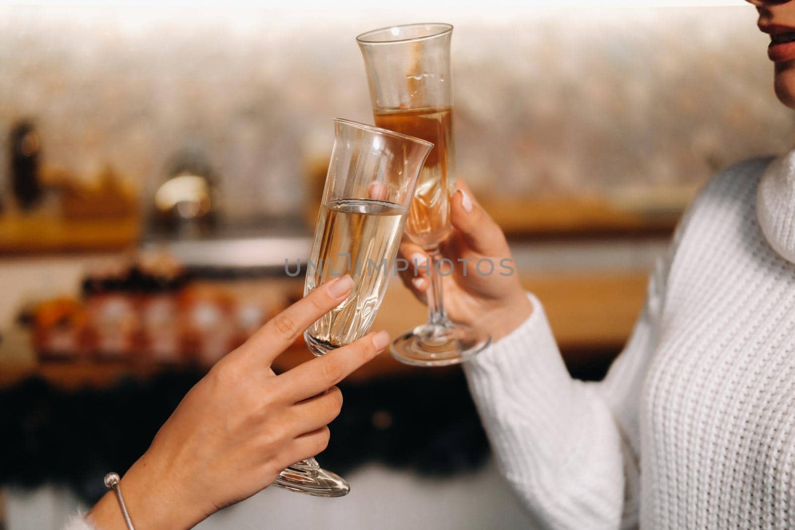 two girls in a cozy home environment with champagne in their hands at Christmas. Smiling girls drink champagne on a festive evening.