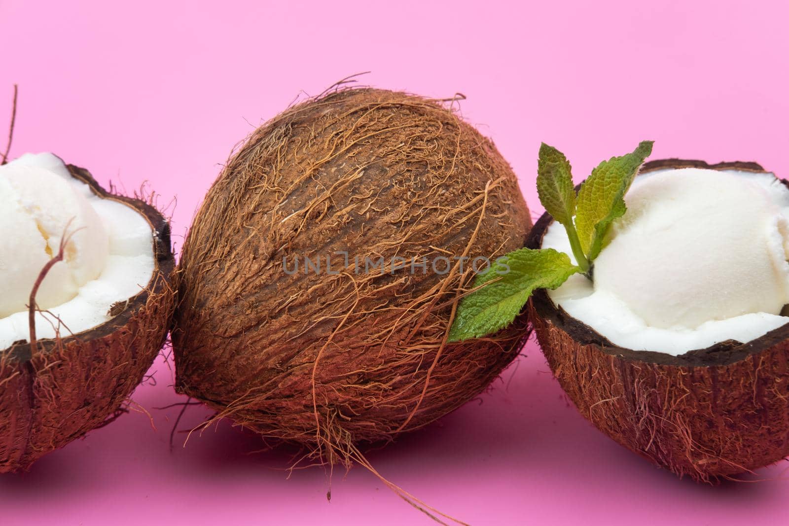 Vanilla ice cream balls in fresh coconut halves decorated with mint leaves on a pink background.