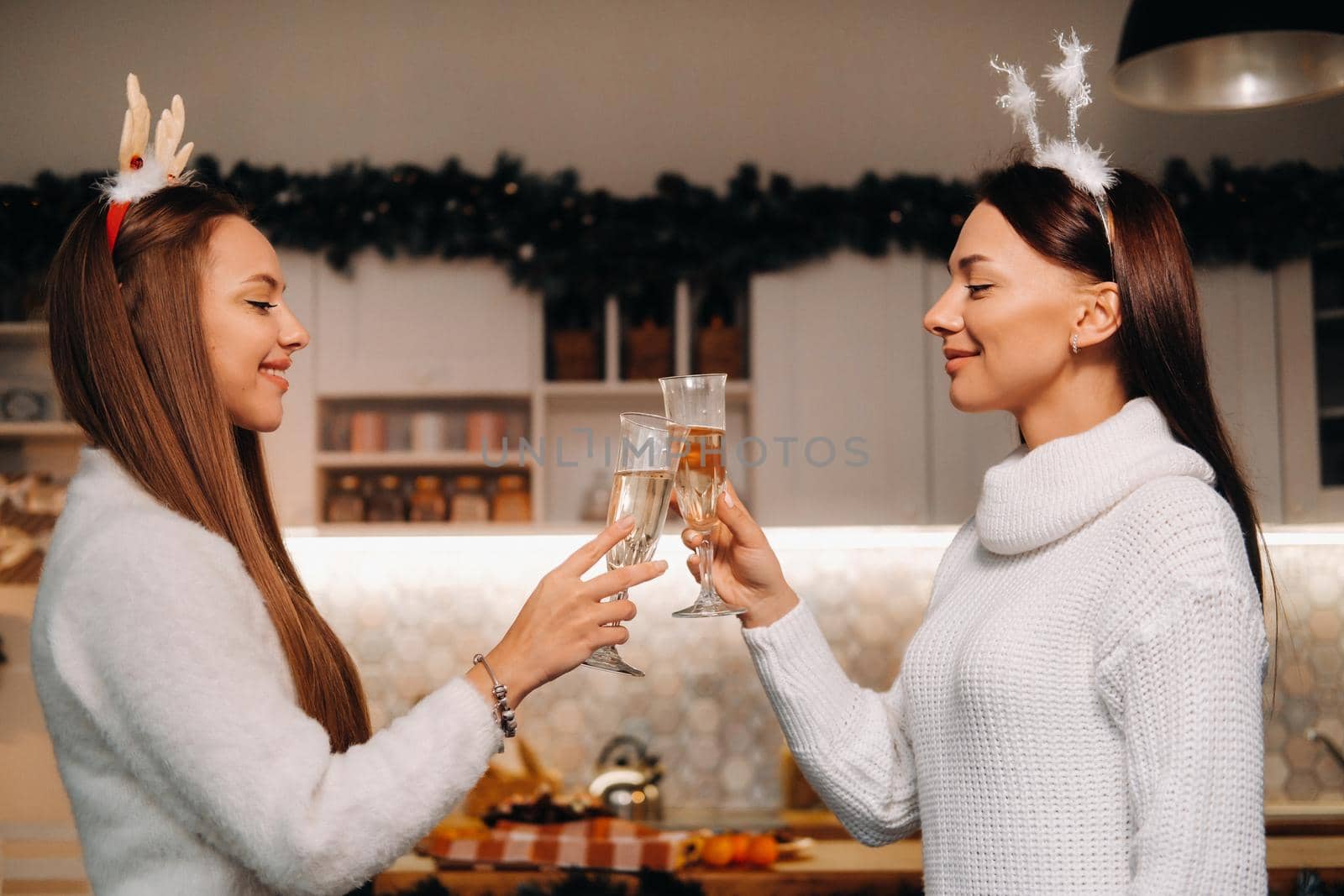 two girls in a cozy home environment with champagne in their hands at Christmas. Smiling girls drink champagne on a festive evening by Lobachad