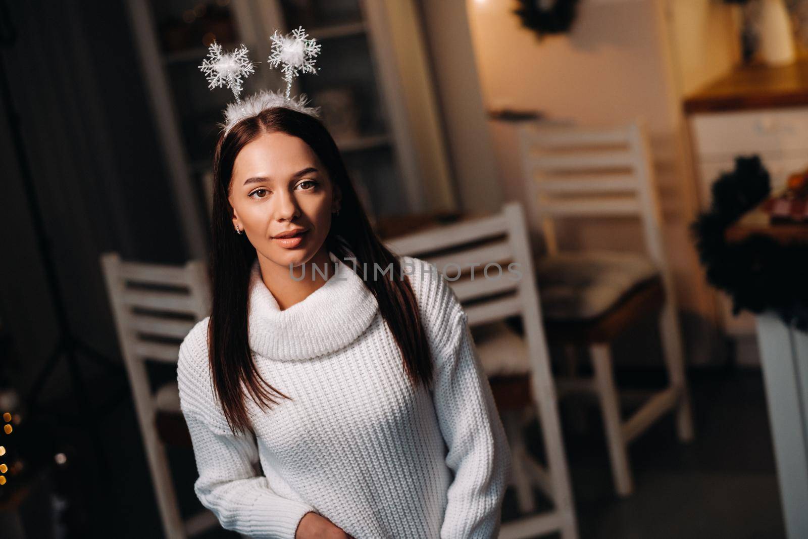 Girl at Christmas with horns in the home interior.A woman on New year's eve in a white sweater by Lobachad