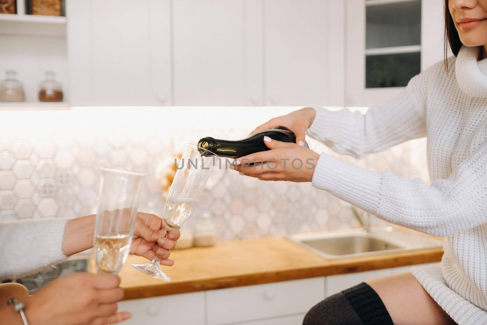 two girls in a cozy home environment in the kitchen pour champagne for Christmas. Smiling girls drink champagne on a festive evening by Lobachad