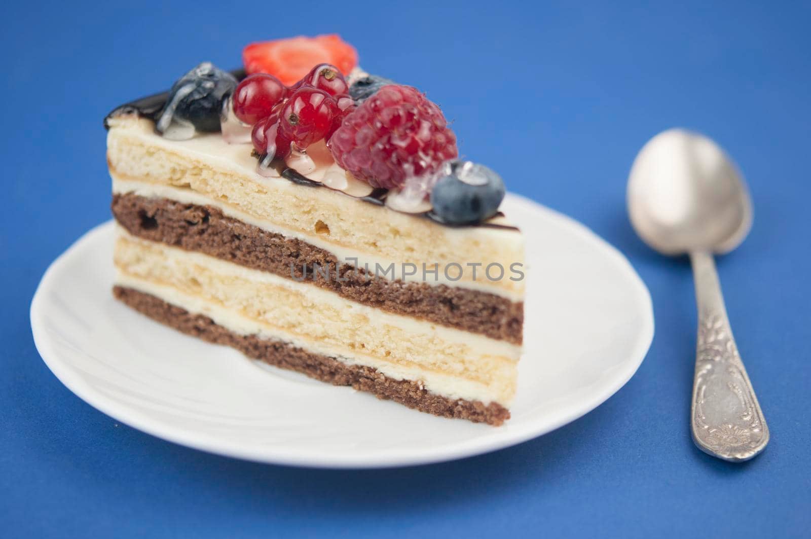 Mix berry slice cake on plate with vintage spoon on soft blue paper background. Good morning. Breakfast