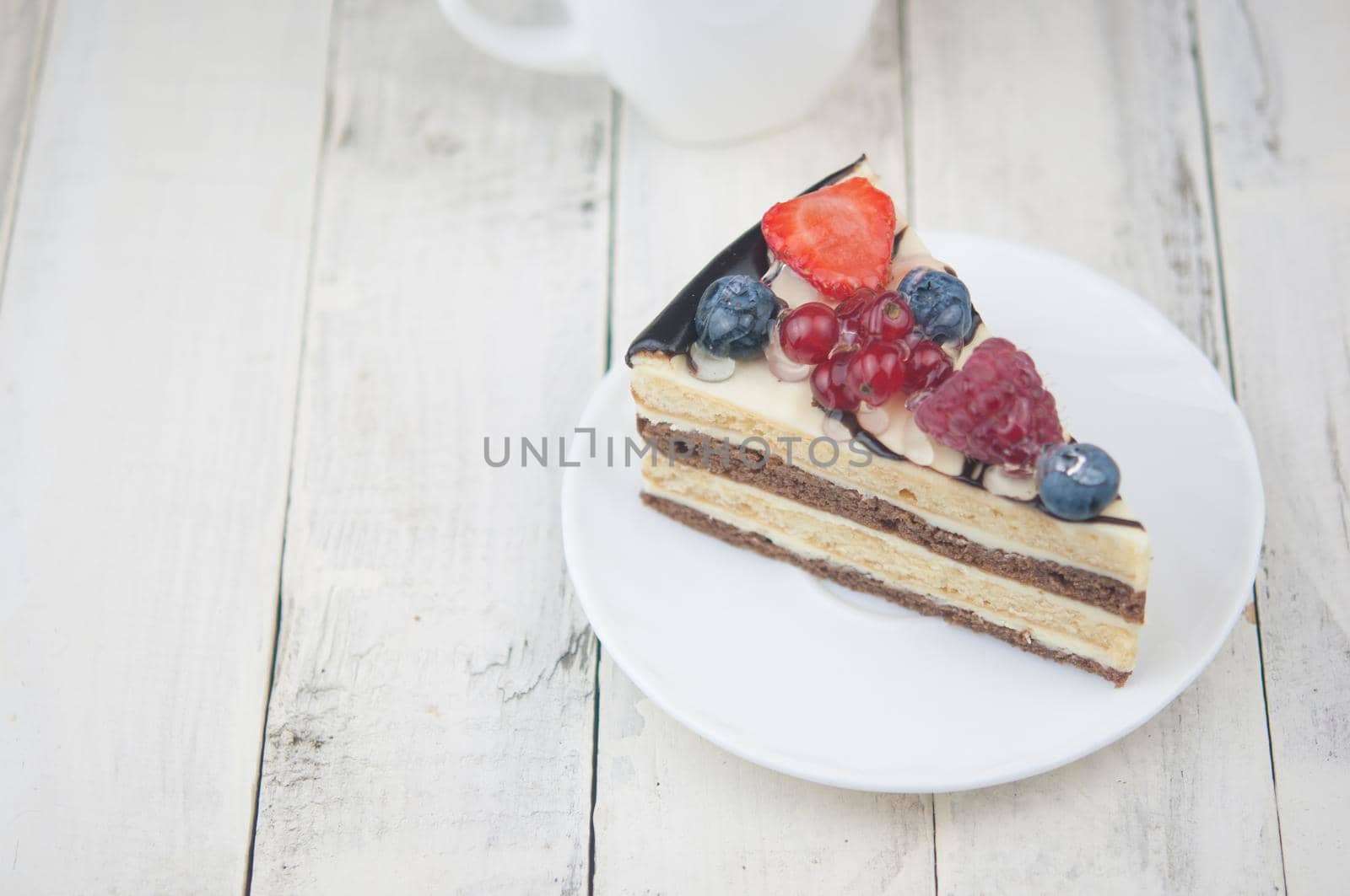 Mix berry colorful slice cake on white plate on wood background