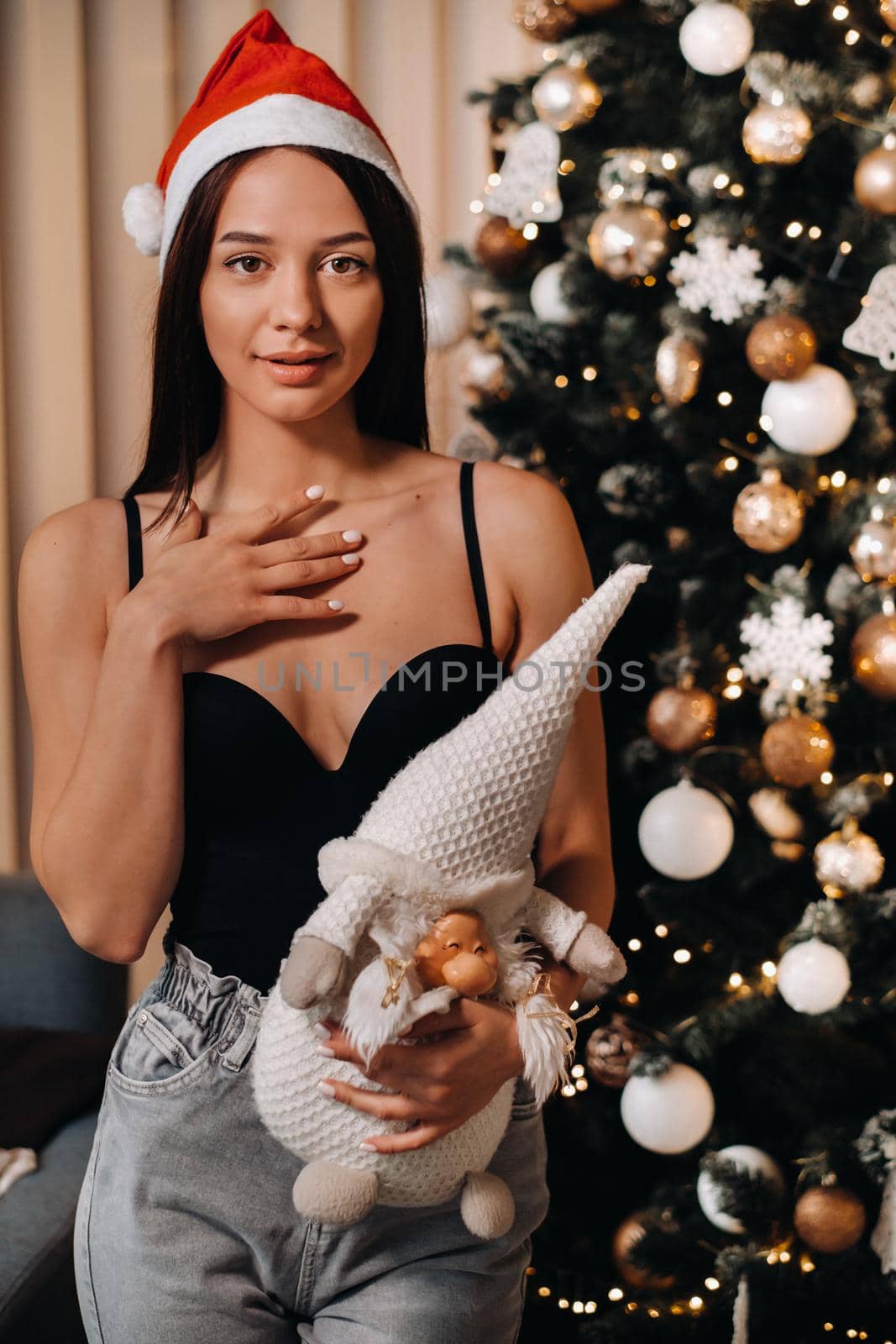 A girl with a toy in her hands stands at home near the Christmas tree.