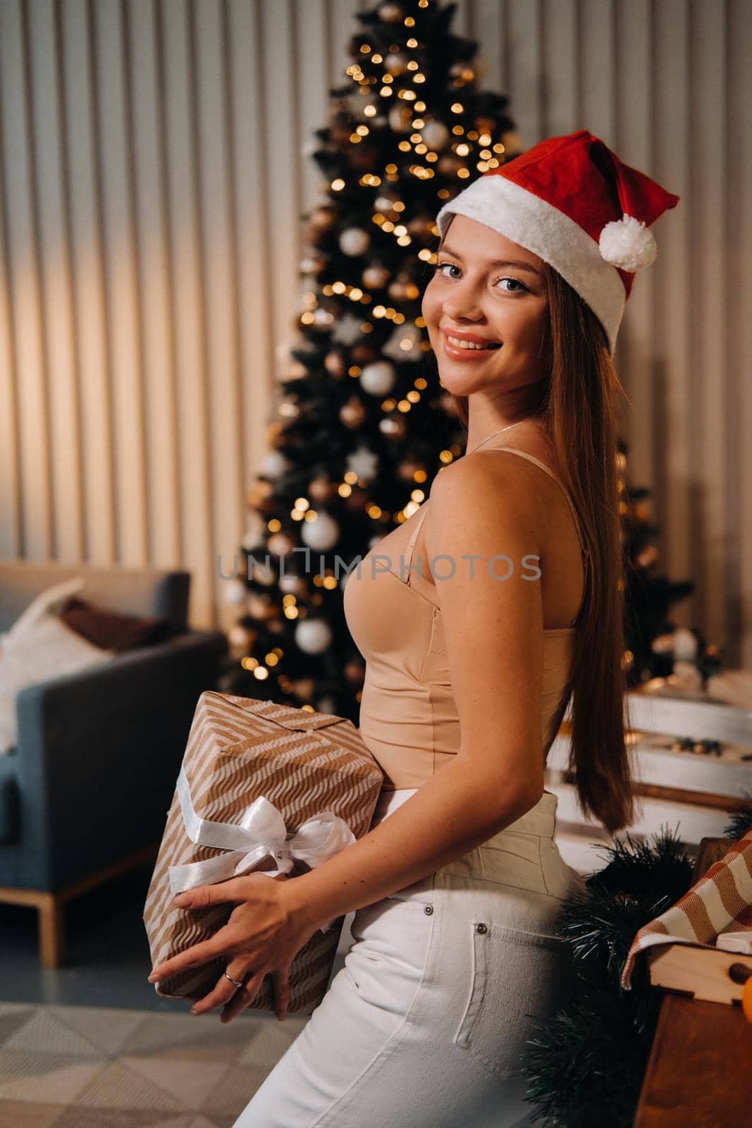 a girl with a new year's gift in her hands stands against the background of a Christmas tree in the interior by Lobachad