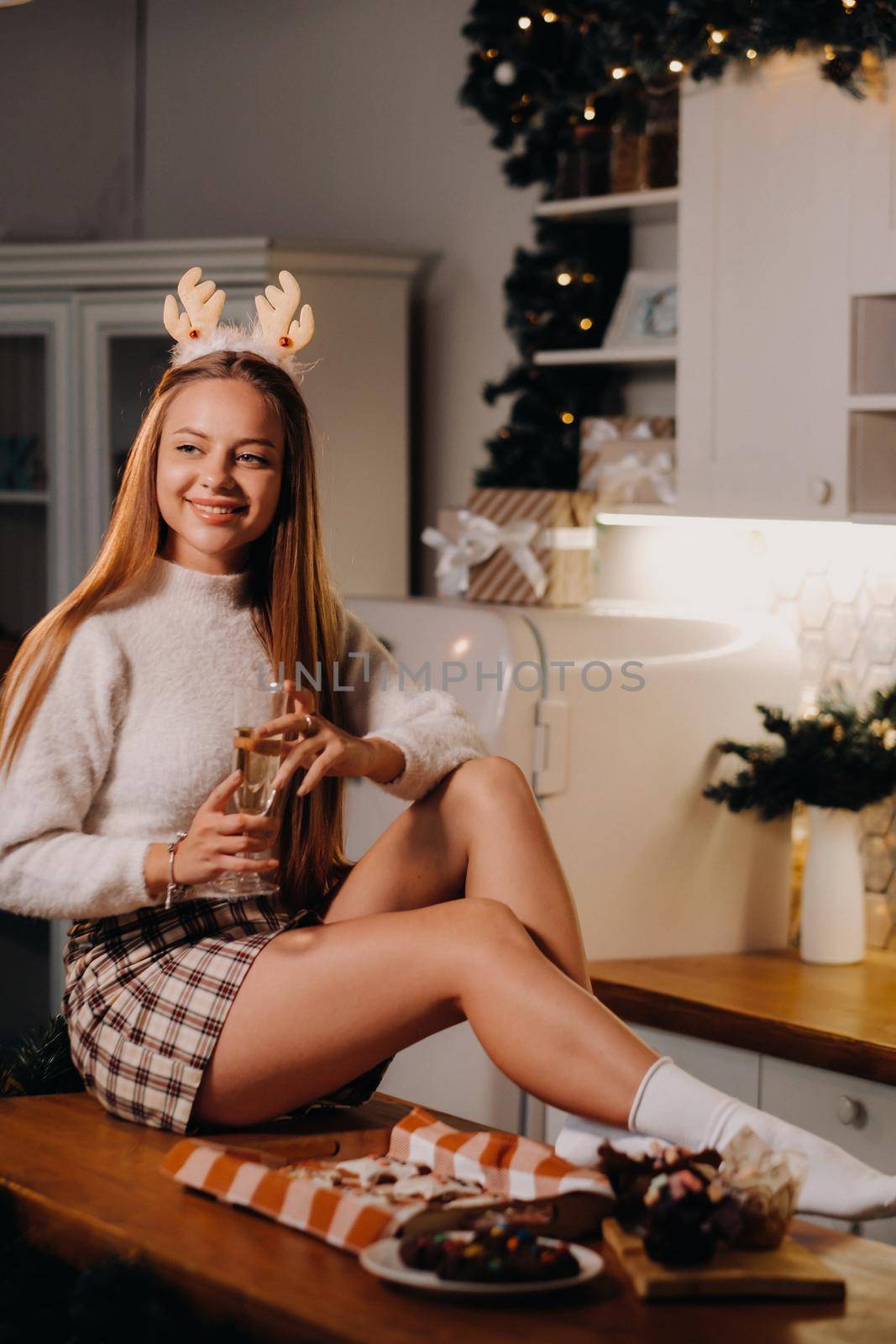 A girl on Christmas day sits on the kitchen table and holds a glass of champagne in her hands.A woman on New year's eve in the kitchen with champagne.