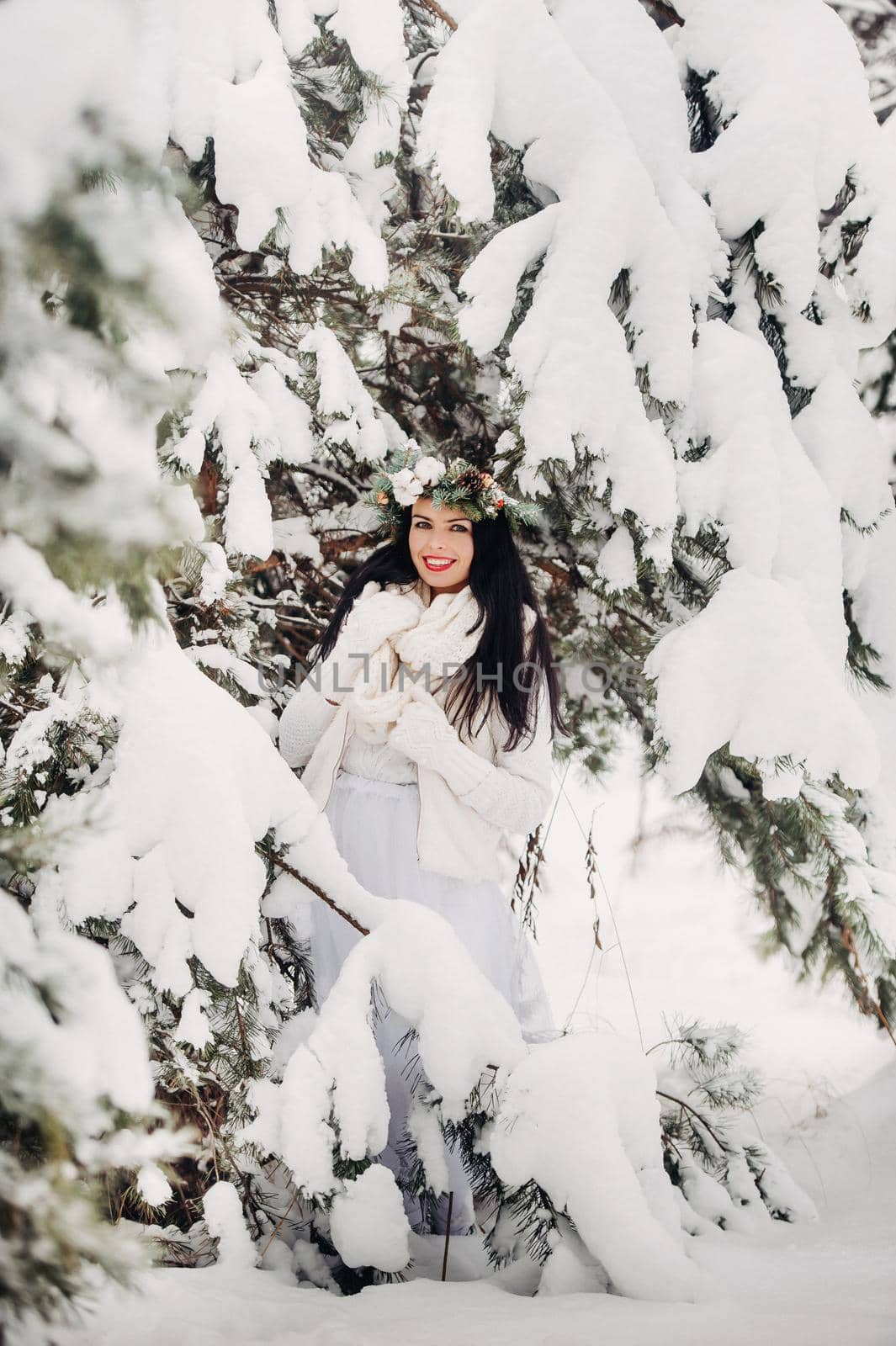 PPortrait of a woman in white clothes in a cold winter forest. Girl with a wreath on her head in a snow-covered winter forest.