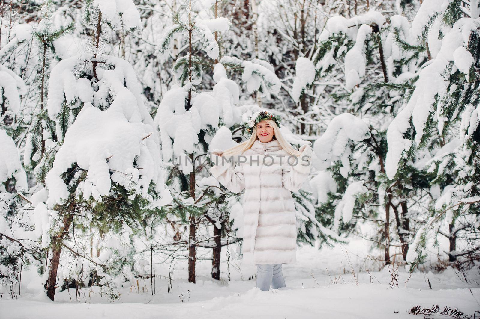 Portrait of a woman in a white fur coat in a cold winter forest. Girl with a wreath on her head in a snow-covered winter forest.