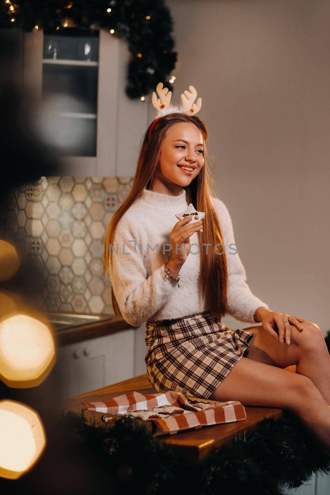 A girl on Christmas day is sitting on the kitchen table and holding cookies in her hands.Woman on new year's eve in the kitchen.