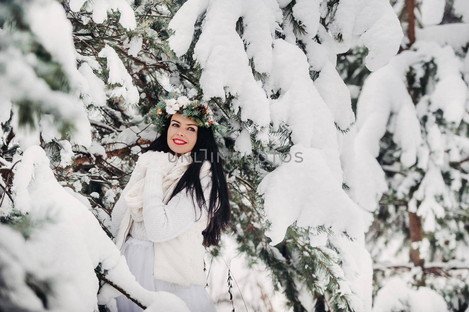 PPortrait of a woman in white clothes in a cold winter forest. Girl with a wreath on her head in a snow-covered winter forest.