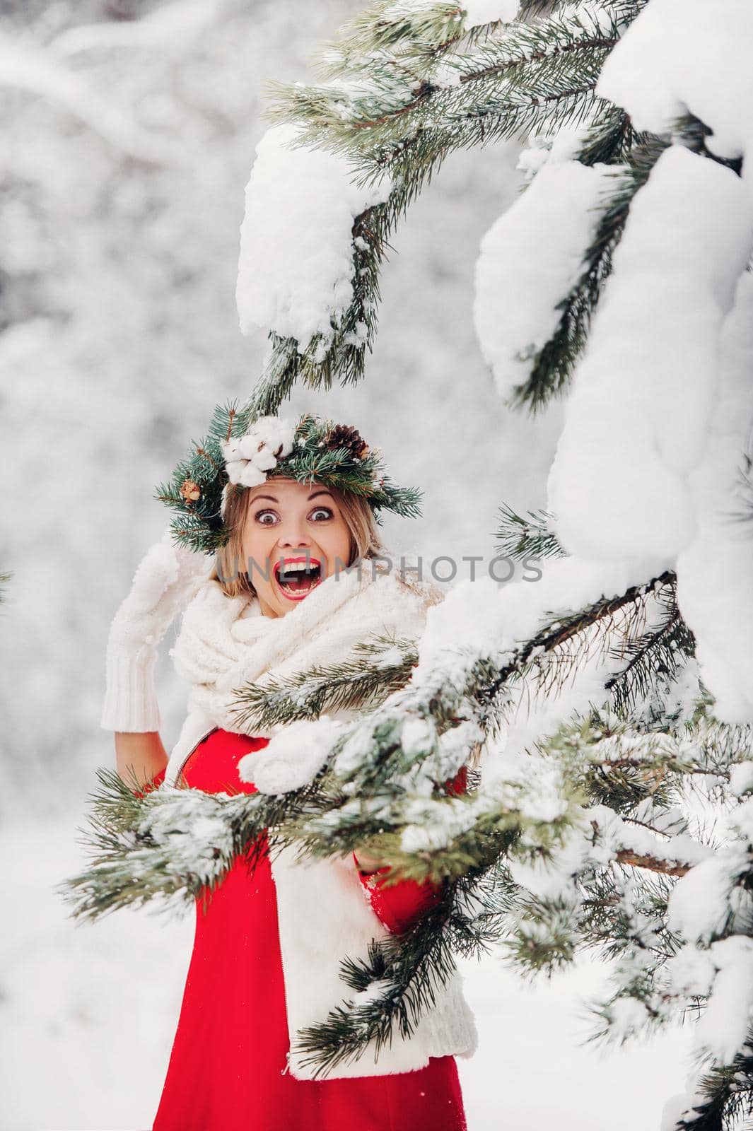 Portrait of a woman in a red jacket in a cold winter forest. Girl with a wreath on her head in a snow-covered winter forest.