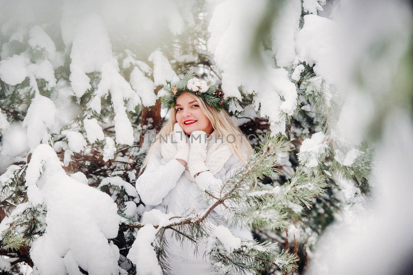 PPortrait of a woman in white clothes in a cold winter forest. Girl with a wreath on her head in a snow-covered winter forest.