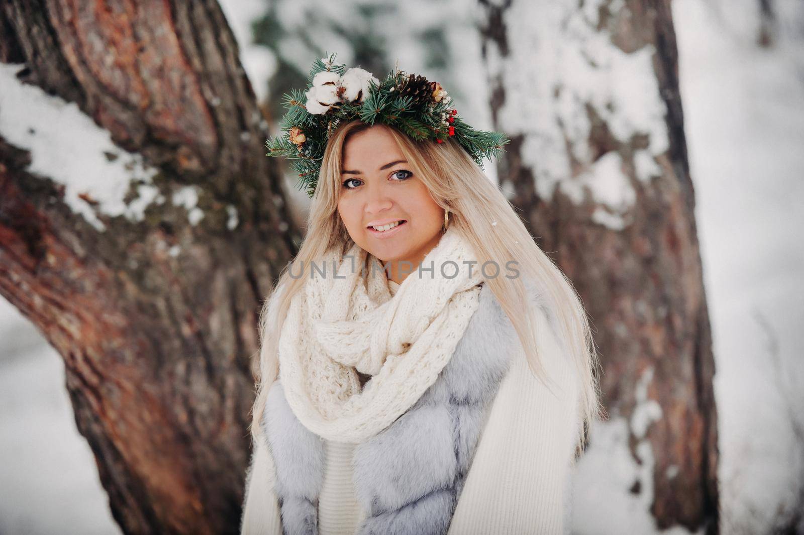 Portrait of a woman in a white fur coat in a cold winter forest. Girl with a wreath on her head in a snow-covered winter forest.