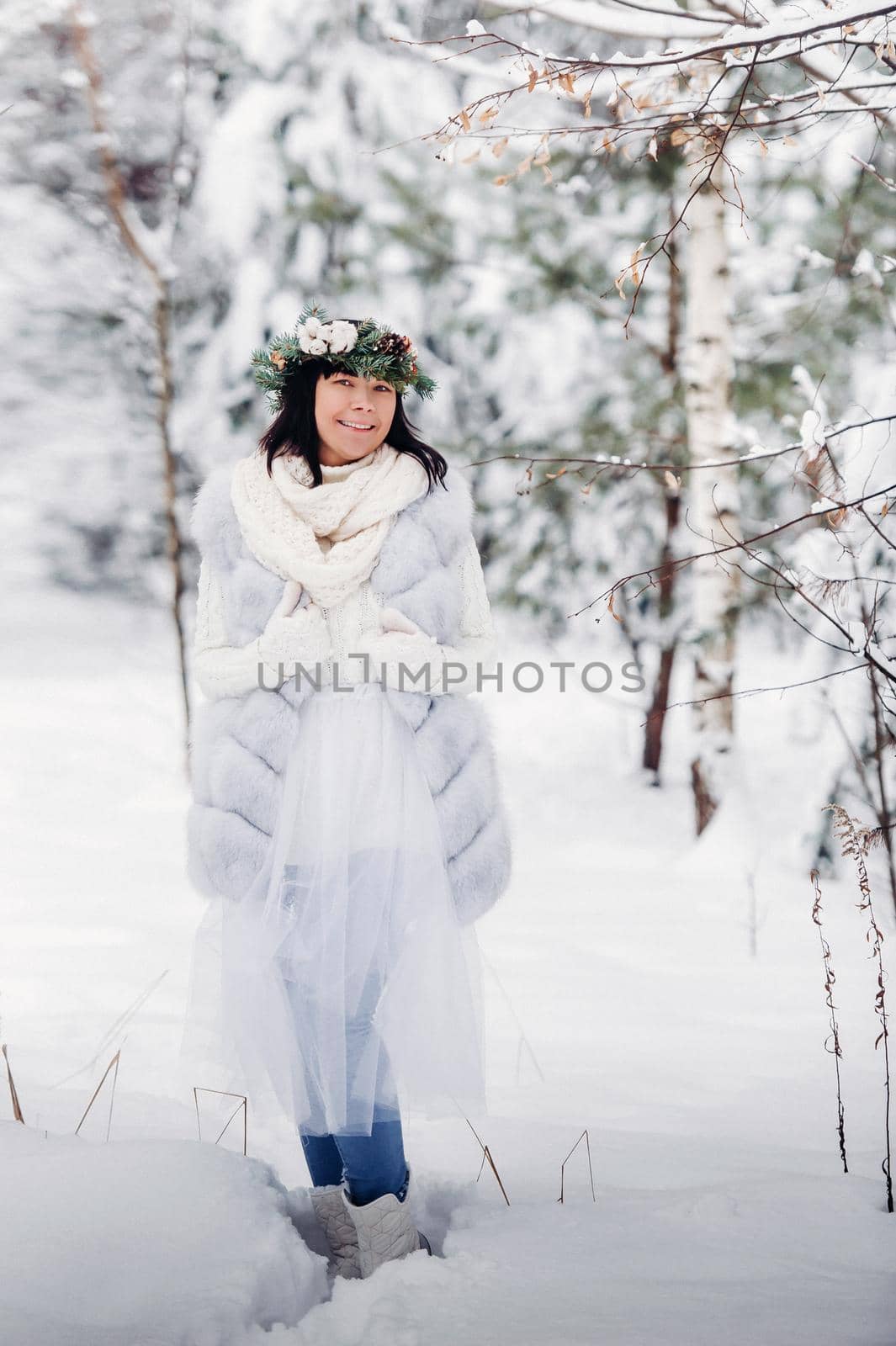 Portrait of a woman in white clothes in a cold winter forest. Girl with a wreath on her head in a snow-covered winter forest