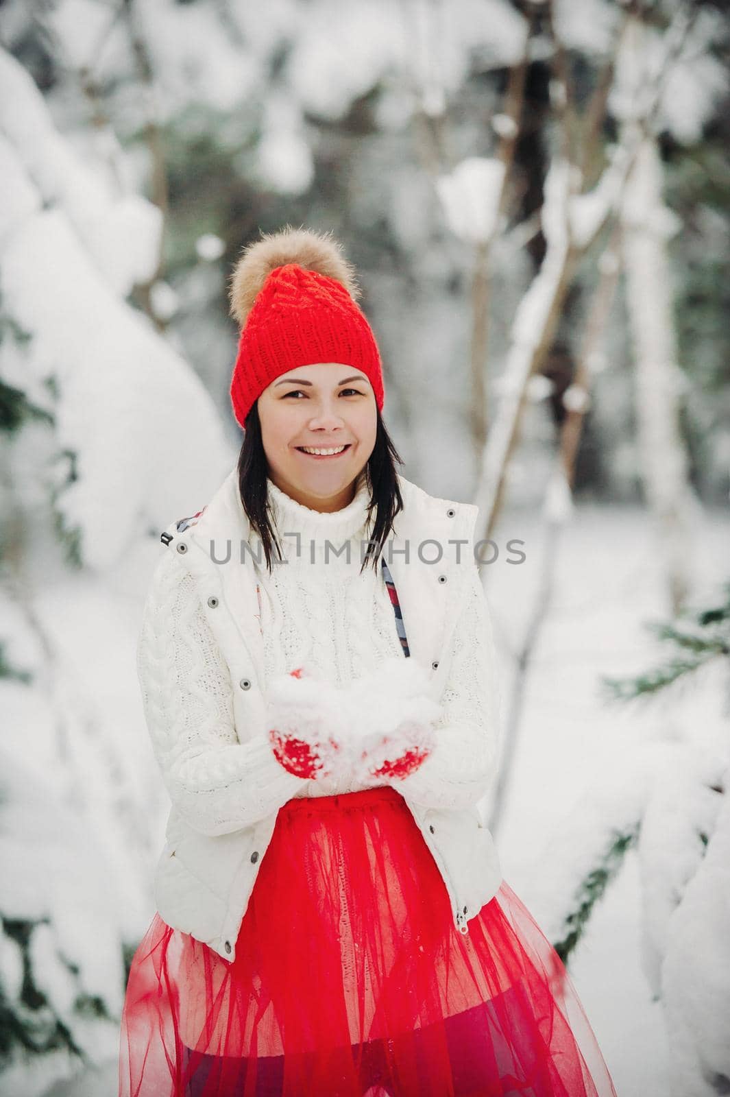 Portrait of a woman in white clothes and a red hat in a cold winter forest. Girl in a snow-covered winter forest.