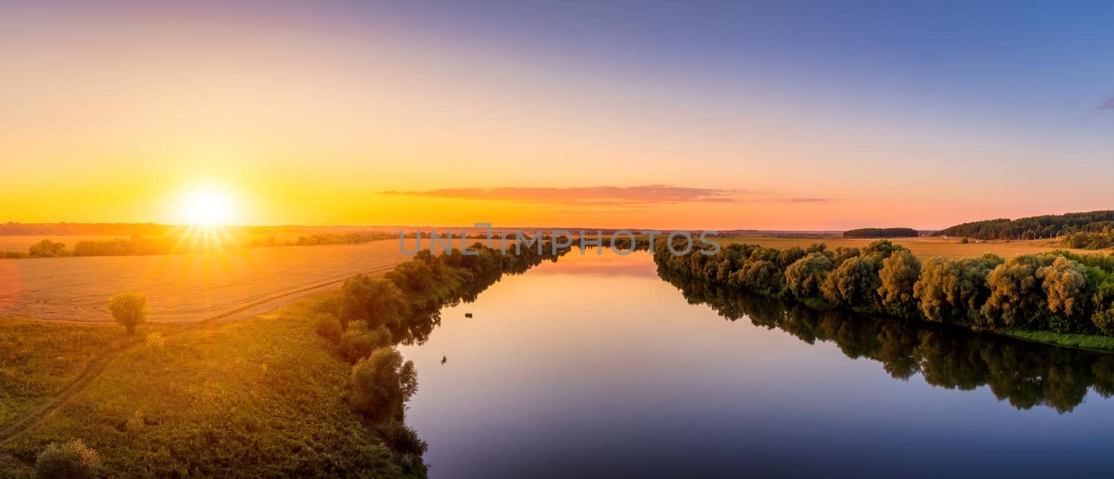 A sunset or sunrise scene over a lake or river with skies reflecting in the water on a summer evening or morning. Panorama.