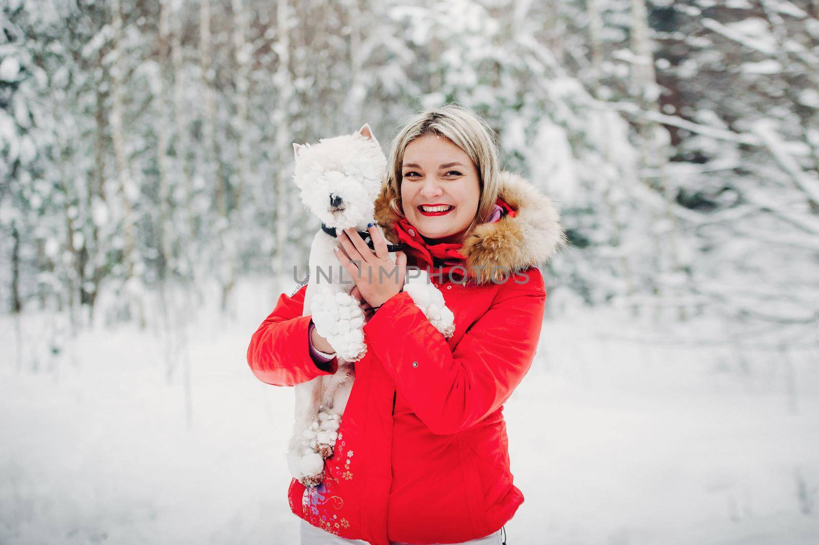 Portrait of a woman in a red jacket with a dog in a cold winter forest. A girl holds a dog in her hands in a snow-covered winter forest