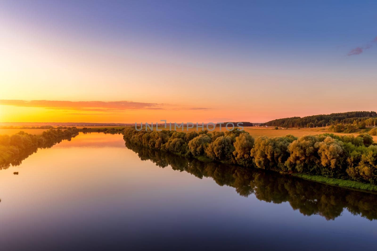 A sunset or sunrise scene over a lake or river with skies reflecting in the water on a summer evening or morning. Landscape.