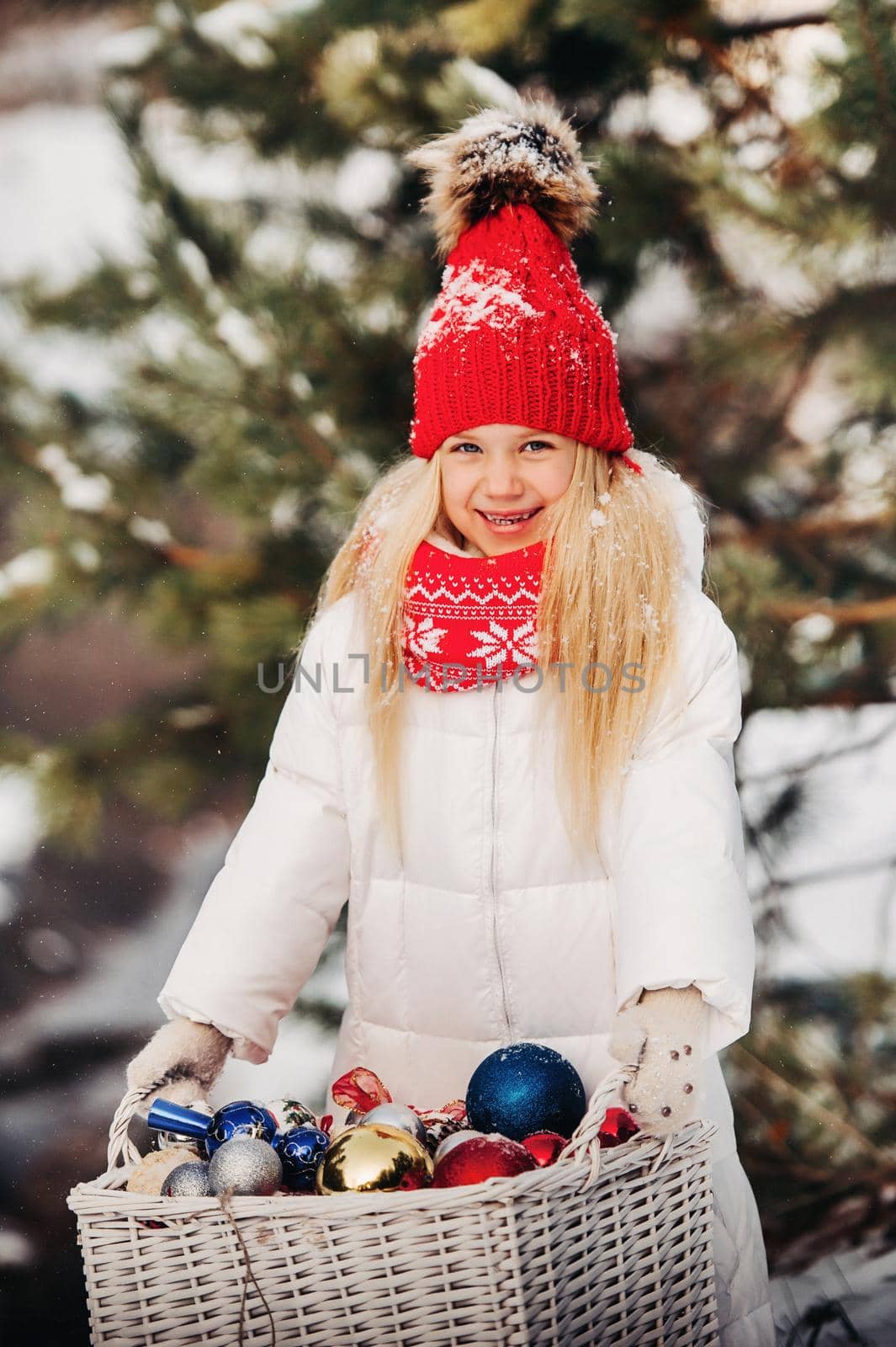 little girl with a basket of Christmas balls near the Christmas tree.Girl with gifts in the winter forest.