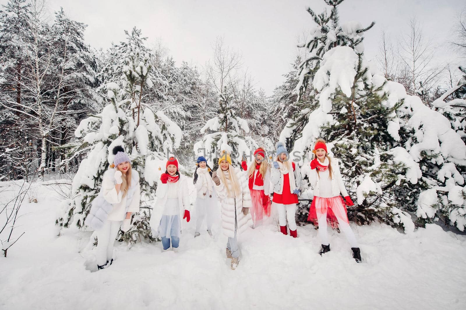 A large group of girls with lollipops in their hands stands in the winter forest.Girls in red and white clothes with candy in a snow-covered forest. by Lobachad