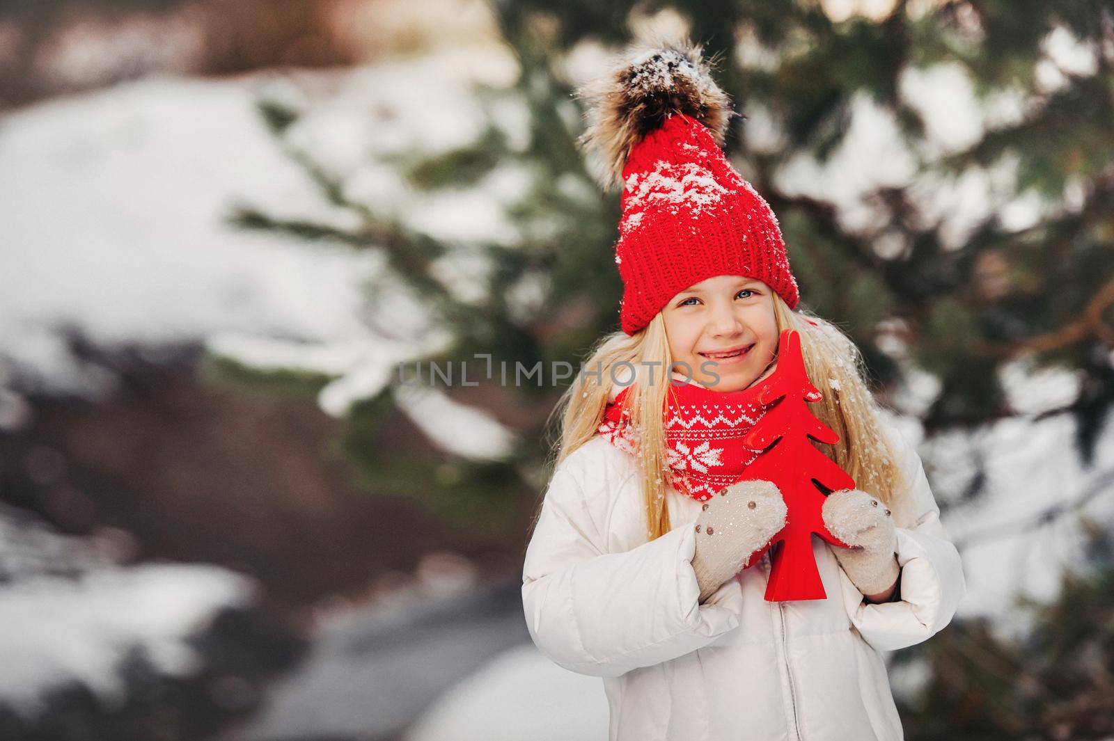 a little girl with a red Christmas tree in her hands in winter on the street.girl with a Christmas tree on a postcard