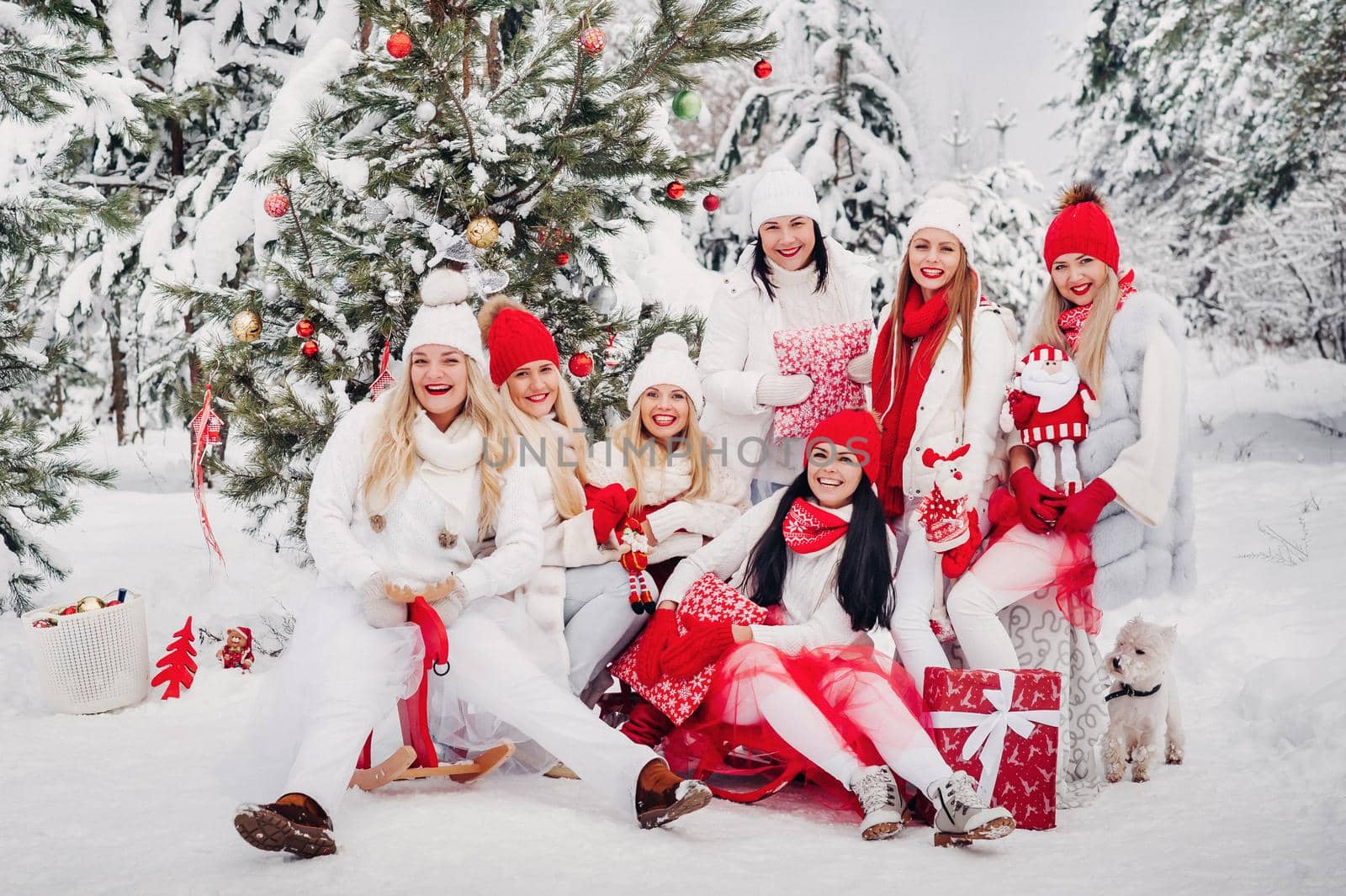 A large group of girls with Christmas gifts in their hands standing in the winter forest.Girls in red and white clothes with Christmas gifts in the snowy forest