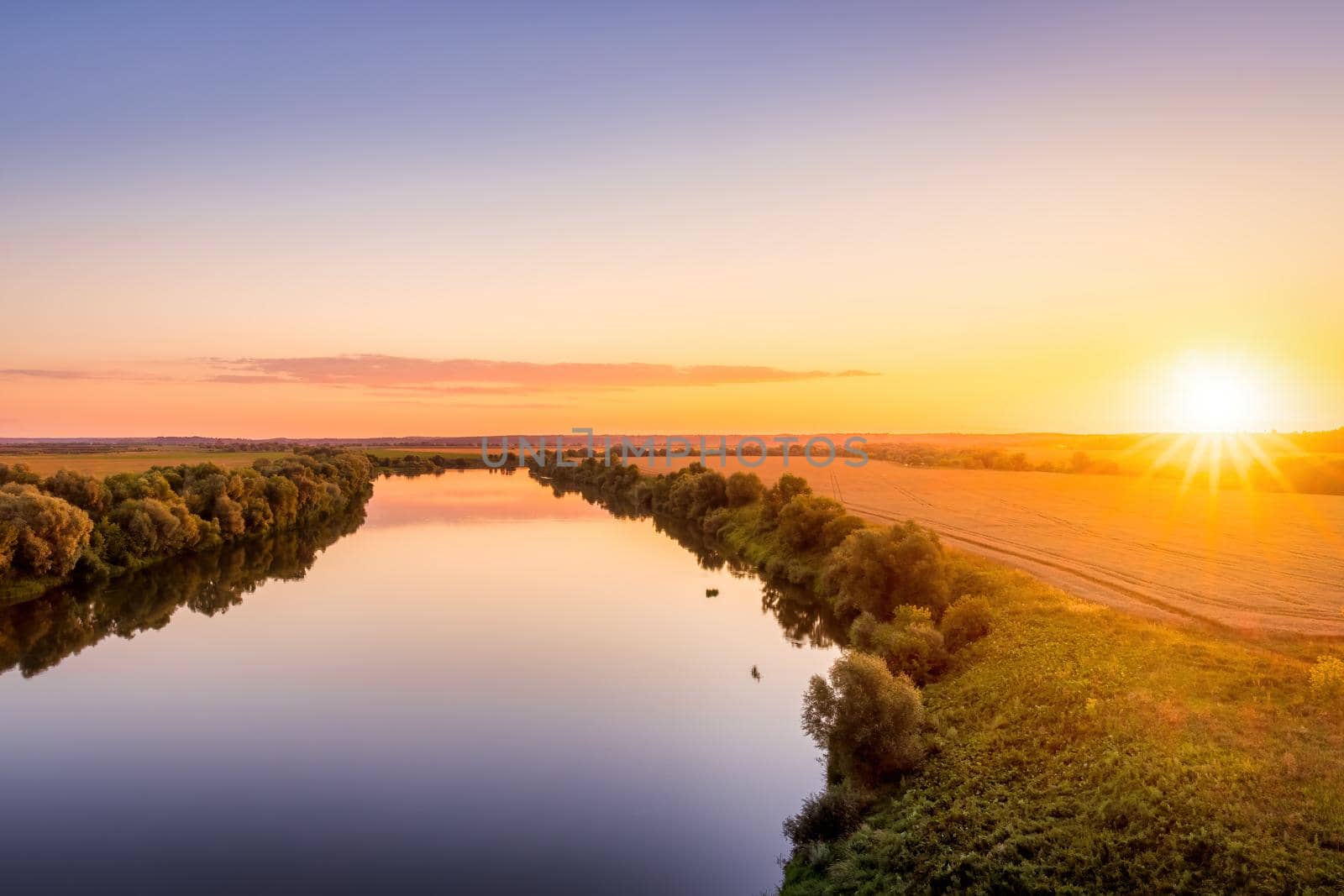 A sunset or sunrise scene over a lake or river with skies reflecting in the water on a summer evening or morning. Landscape.