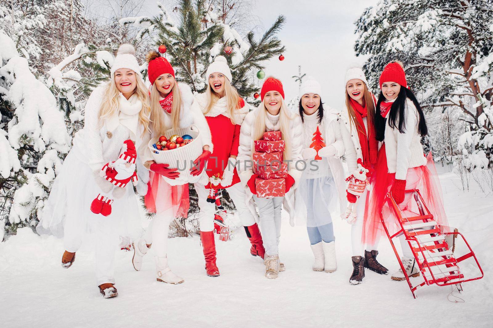 A large group of girls with Christmas gifts in their hands standing in the winter forest.Girls in red and white clothes with Christmas gifts in the snowy forest by Lobachad