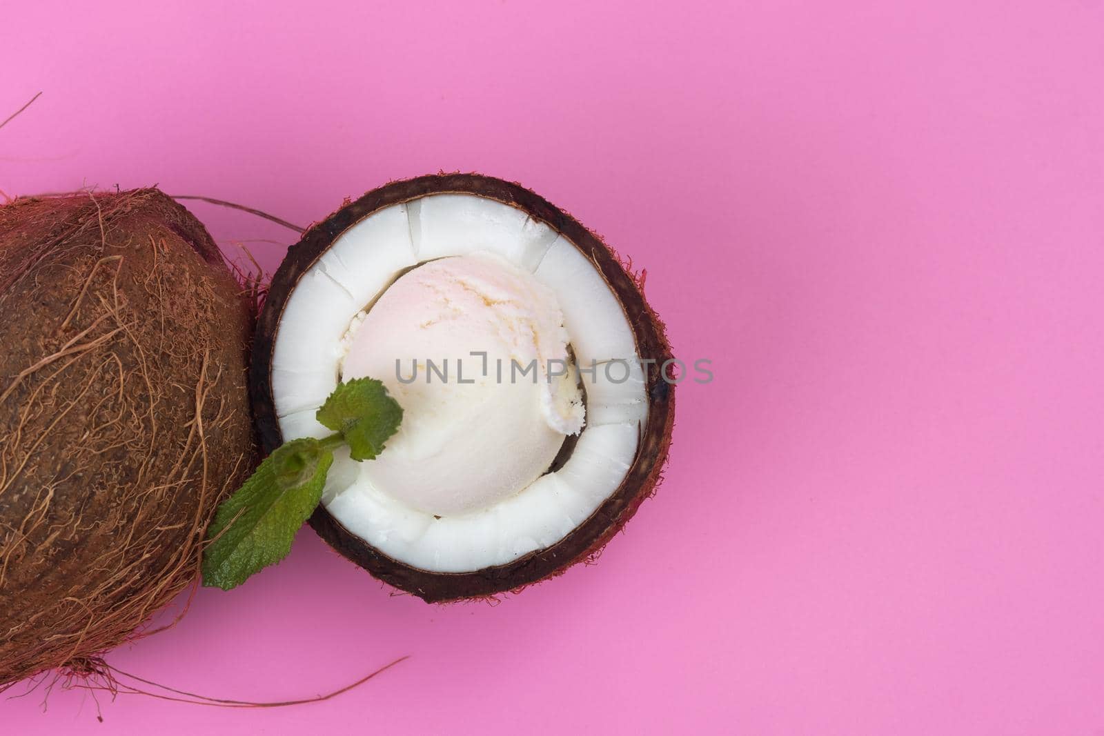 Vanilla ice cream balls in fresh coconut halves decorated with mint leaves on a pink background.